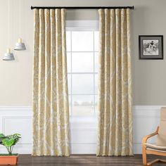 a living room with a chair and window covered in yellow floral curtain panels next to a potted plant