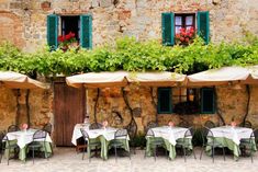 an outdoor dining area with tables, chairs and umbrellas set up outside in front of a stone building