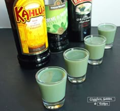 four shot glasses filled with green liquid next to two bottles of kahlu beer