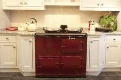 a red stove top oven sitting inside of a kitchen next to white cabinets and counter tops