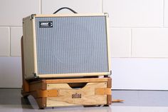 an old guitar amplifier sitting on top of a wooden box with wheels and handles, in front of a white brick wall