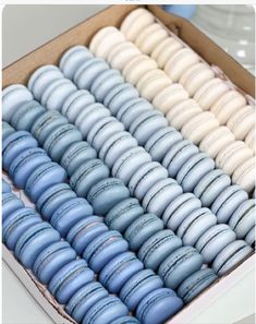 an open box filled with blue and white macaroons on top of a table