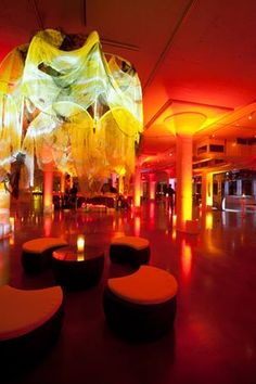 a room filled with lots of tables and chairs covered in yellow cloths, lit by colorful lights