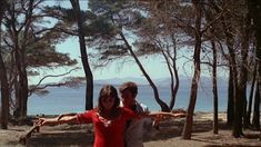 two people standing in front of trees with their arms spread out and one person pointing at the camera