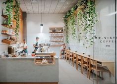 the interior of a coffee shop with plants hanging from the ceiling and people sitting at tables