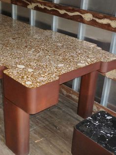 a wooden table with two metal legs and a marble top in front of some windows