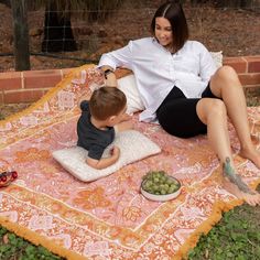 a woman sitting on top of a blanket next to a little boy