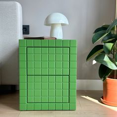 a green tiled cabinet next to a mushroom lamp and potted plant on the floor