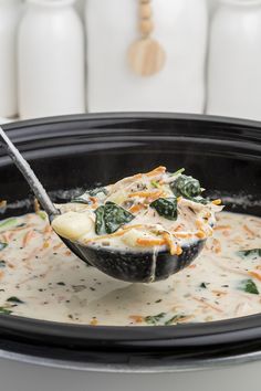 a spoon full of soup with spinach and cheese on it in a crock pot