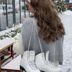 a woman holding two white ice skates in front of a building with snow on the ground