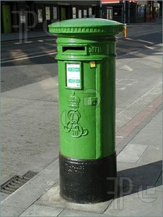 a green post box sitting on the side of a street