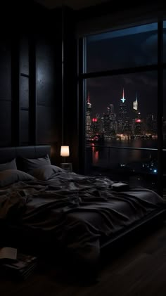 a large bed in a dark room next to a window with the city lights lit up