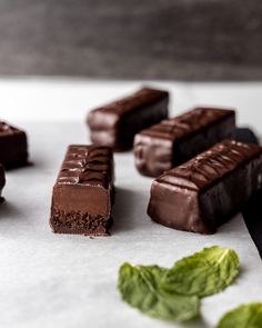 several pieces of chocolate sitting on top of a white surface next to green leafy leaves