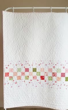 a white quilt hanging from a shower curtain with red and green squares on the border