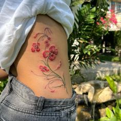 a woman's lower back tattoo with pink flowers on her stomach and behind her is a pond