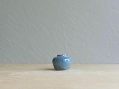 a small blue vase sitting on top of a wooden table next to a white wall