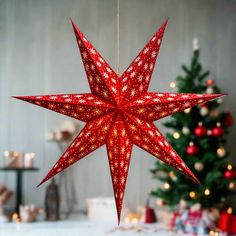 a red star ornament hanging from a string in front of a christmas tree