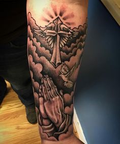 a man's arm with a cross and praying hands in the clouds on it