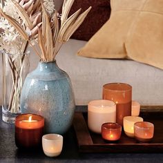 candles are arranged on a tray next to a vase with dried flowers and grasses in it