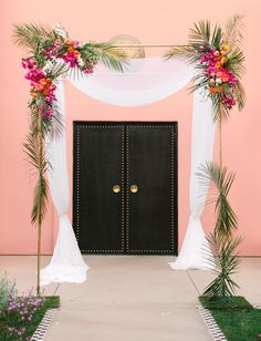 a black door with white drapes and pink flowers on the side is surrounded by greenery