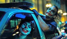 a man with makeup on his face sitting in a car next to a woman dressed as the joker