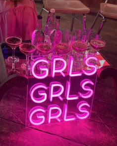 there is a neon sign that says girls girls and wine glasses on the table in front of it