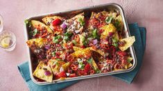 a pan filled with nachos on top of a blue cloth next to two glasses