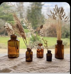 three brown glass vases with dried plants in them on a tableclothed surface