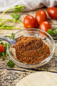 a glass bowl filled with seasoning next to some tomatoes and pita bread on a wooden table