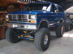 a large blue truck parked in a garage next to a car with big tires on it