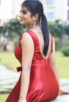 a woman in a red dress is sitting on a ledge and looking off into the distance