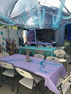 an outdoor dining area with blue and purple table cloths, white chairs, and tables