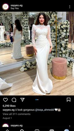 a woman standing in front of a mirror wearing a white dress with long sleeves and sheer neckline