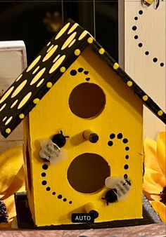 a yellow birdhouse with bees and polka dots painted on it's side, next to flowers