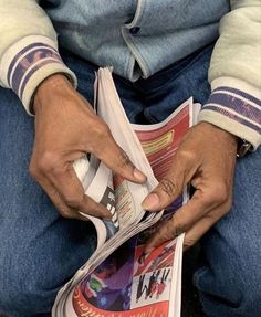 a person sitting down reading a newspaper with their hands on the front page and holding it