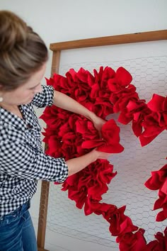 a woman is making a heart out of red ruffles on a white board