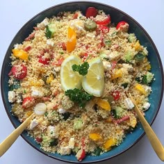 a blue bowl filled with couscous and lemon wedges next to two wooden spoons