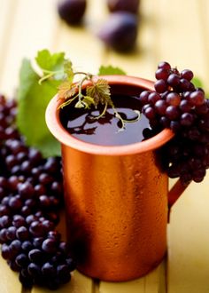 some grapes are next to a copper cup with liquid in it on a wooden table