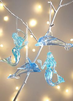 three glass ornaments hanging from branches with lights in the background