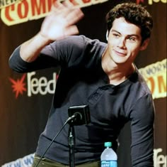 a young man is giving a speech in front of a microphone with his hand up