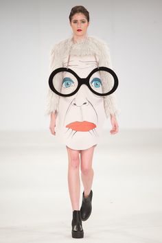 a woman with glasses on her face walks down the runway in a white dress and fur coat