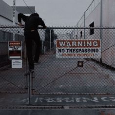 a man standing on top of a fence next to a no trespassing sign