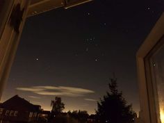 the night sky is lit up with stars and clouds in the distance as seen from an open window