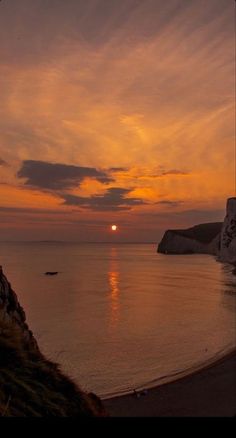 the sun is setting over the ocean with cliffs in the foreground and people walking on the beach below