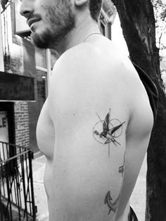 a man with a small tattoo on his chest standing in front of a tree and looking off into the distance