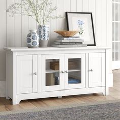 a white entertainment center with books and vases on the top, next to a rug