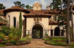 the front entrance to a large home with lots of greenery and flowers on either side