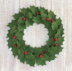 a christmas wreath with holly leaves and red berries hanging on a white wooden background,