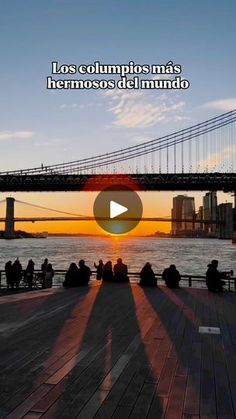 people are sitting on the dock watching the sun go down over the bay bridge in san francisco, california