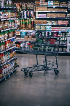 an empty shopping cart in the middle of a grocery store filled with drinks and condiments